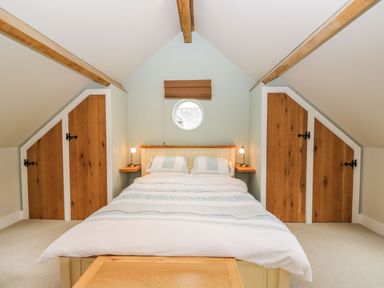 A bedroom with a double bed under a pitched ceiling with wooden beams and four wooden cupboard doors at Avon Turn View in Alderbury