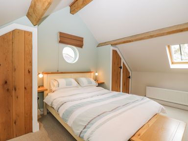 A bedroom with a double bed, wooden beams, circular window, wooden doors, and a skylight at Avon Turn View in Alderbury