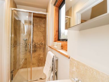 A bathroom with a glass shower enclosure a towel rack with towels a window with wooden frame and a sink at Avon Turn View in Alderbury