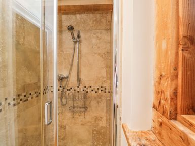 A shower area with tiled walls a handheld showerhead a metal shower caddy and a glass door at Avon Turn View in Alderbury