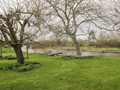 A riverside garden with trees a wooden bench and table on a small dock at Avon Turn View in Alderbury