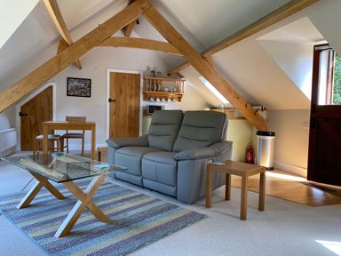 An attic living room with leather sofa glass coffee table wooden dining table and exposed wooden beams at Avon Turn View in Alderbury