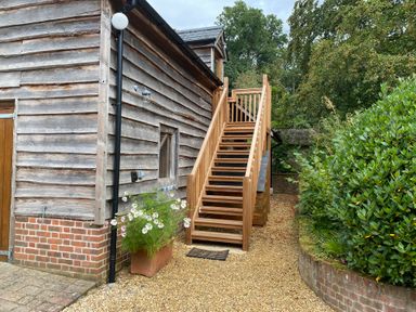 An exterior wooden staircase next to a wooden building with a brick base and a planter with flowers at Avon Turn View in Alderbury