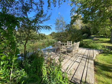 A wooden deck with chairs and a table next to a pond surrounded by trees and greenery at Avon Turn View in Alderbury