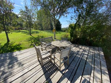 An outdoor wooden deck with a table and chairs surrounded by trees and grass at Avon Turn View in Alderbury