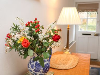 A table with a floral arrangement in a blue and white vase and a lamp near a white door at Riseholme in Ebberston