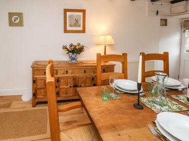 A dining room with wooden table and chairs set with plates and glasses and a wooden sideboard with flowers and a lamp Riseholme Ebberston
