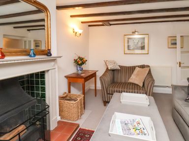 A living room with a fireplace a small wooden table with a vase of flowers a striped armchair a sofa and a coffee table with trays at Riseholme in Ebberston