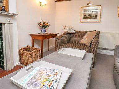 A living room with a striped armchair, a wooden side table with a vase of flowers, white trays on a gray ottoman at Riseholme in Ebberston