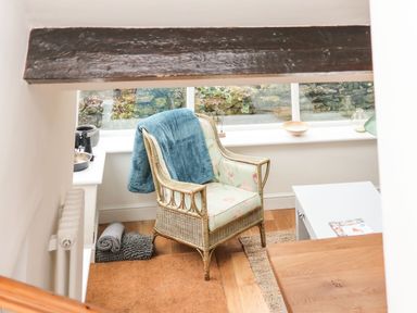 A wicker armchair with a blue blanket draped over it next to a white table and a window at Riseholme in Ebberston