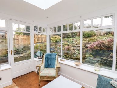 A sunroom with large windows overlooking a garden and a wicker chair with a blue throw at Riseholme in Ebberston