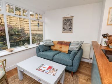 A seating area with a blue sofa with pillows a white coffee table with magazines a framed botanical print and large windows at Riseholme in Ebberston