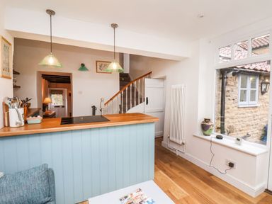 A kitchen area with a wooden countertop and light blue paneling two hanging lights a staircase a large window with a vase and electronic device on the sill at Riseholme in Ebberston