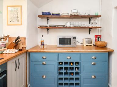 A kitchen area with blue cabinets wooden countertop shelves with dishes and glassware microwave and toaster at Riseholme in Ebberston