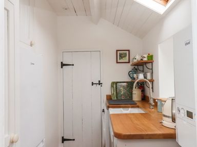 A small utility room with a wooden countertop sink kettle washing machine a door and shelves with teapots and cups at Riseholme Ebberston