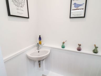 A white corner sink with a soap dispenser and three small vases on a ledge with two framed prints on the walls at Riseholme Ebberston