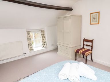 A bedroom with a white wardrobe a wooden chair with striped cushion a small window with floral curtains and a bed with towels at Riseholme in Ebberston