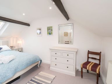 A bedroom with a bed blue bedspread white dresser mirror two framed pictures and a wooden chair at Riseholme in Ebberston