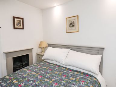 A bedroom with a bed with floral quilt two white pillows a bedside table with lamp a fireplace and two framed pictures on the wall at Riseholme in Ebberston