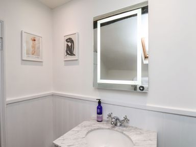 A bathroom sink with a marble countertop a lit rectangular mirror and two framed artworks on the wall at Riseholme in Ebberston