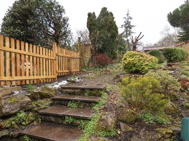 An outdoor garden area with stone steps leading up and various bushes and trees along a wooden fence at Riseholme in Ebberston