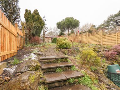 An outdoor garden area with stone steps leading up to a path with wooden fences and trees at Riseholme in Ebberston