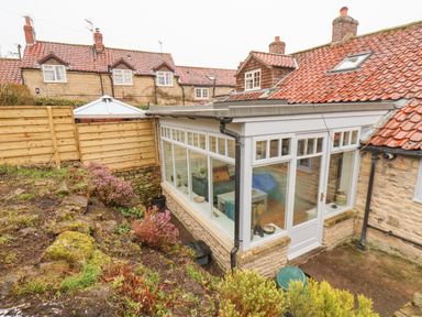 A garden area with plants and a glass conservatory attached to a stone house with a tiled roof at Riseholme in Ebberston