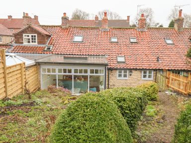 A garden with trimmed bushes and a pathway behind a stone house with tiled roof and skylights at Riseholme in Ebberston