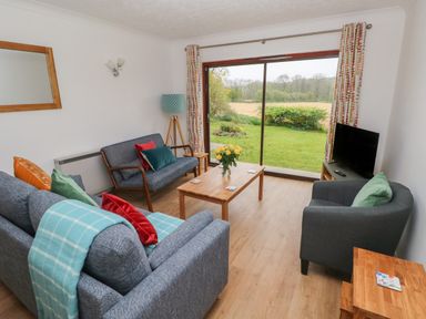 A living room with blue sofas a wooden coffee table and a television near a large sliding glass door at Timaru in Lamphey