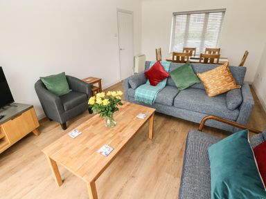 A living room with a wooden coffee table yellow flowers on the table sofas and armchairs with cushions and a dining table with chairs at Timaru in Lamphey