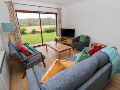 A living room with sofas chairs a coffee table and a television with a view of a garden at Timaru in Lamphey