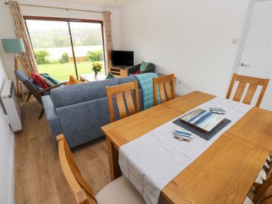 A dining area with wooden table and chairs next to a living area with sofa armchair and television at Timaru in Lamphey