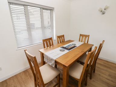 A dining room with a wooden table and six chairs near a window with blinds at Timaru in Lamphey