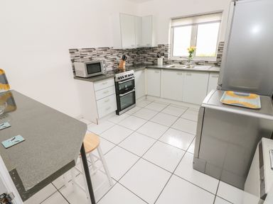 A kitchen with white cabinets a stove a microwave a sink and a refrigerator at Timaru in Lamphey