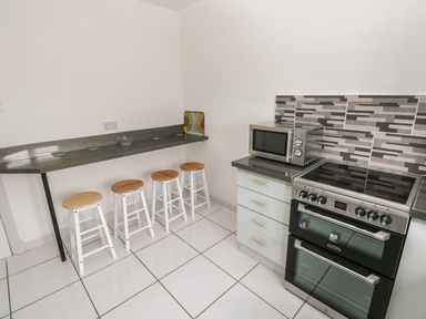A kitchen with a stove, microwave, counter with stools, and tiled floor at Timaru in Lamphey