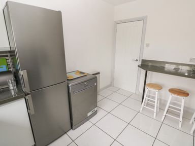 A kitchen area with a gray refrigerator and dishwasher next to a counter with two stools at Timaru in Lamphey