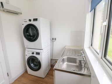 A laundry room with a washer and dryer stacked and a metal sink next to a window at Timaru in Lamphey