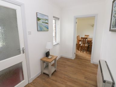 A hallway with a small table holding a lamp and radio leading to a dining room with a wooden table and chairs at Timaru in Lamphey