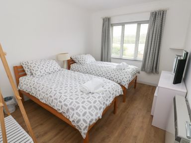 A bedroom with two single beds with patterned bedding a white bedside lamp a window with patterned curtains and a white dresser with a TV at Timaru Lamphey