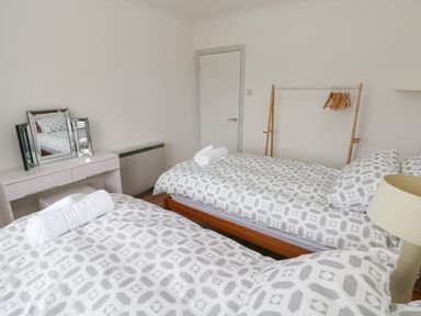 A bedroom with two single beds a vanity table a mirror and a wooden clothes rack at Timaru in Lamphey