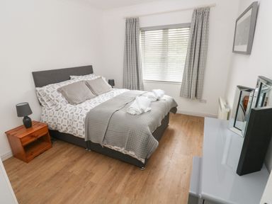 A bedroom with a double bed bedside table lamp window with curtains and a dresser with mirrors at Timaru in Lamphey