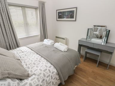 A bedroom with a bed with gray and white bedding a dressing table with a mirror and a wall picture at Timaru in Lamphey