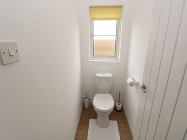 A small bathroom with a white toilet, a window with a yellow blind, a toilet brush, and toilet paper holders at Timaru in Lamphey