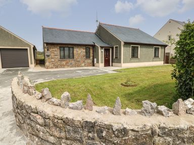 A single story house with stone and plaster walls a garage driveway and a grassy front yard at Timaru in Lamphey