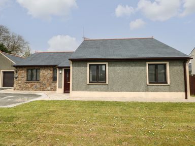 A single-story house with stone and plaster exterior walls two windows and a brown door with a garage on the side at Timaru in Lamphey