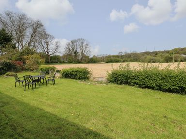 A garden with a metal table and four chairs on grass facing a field and trees at Timaru in Lamphey