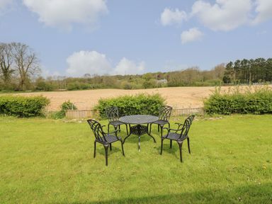 A metal outdoor table with four chairs on a grassy lawn with fields and trees in the background at Timaru in Lamphey