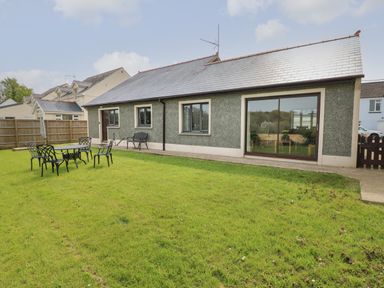 A garden with patio furniture and a single-story house with a gray roof and sliding glass door at Timaru in Lamphey
