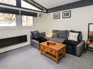 A living room with a gray sofa and a wooden coffee table under windows at 64 Penlan Holiday Park in Cenarth