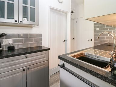 A kitchen with grey cabinets black countertop a sink with a faucet grey tiled backsplash and white doors at 64 Penlan Holiday Park in Cenarth